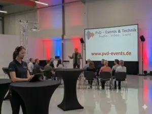 Seminar- und Konferenztechnik-Setup von PvD Events in einem modernen Showroom in OWL mit Beamer, Großleinwand, Publikum und Technikerin am Tablet.