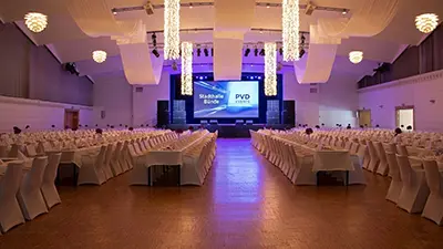 Professionelles Event-Setup von PvD - Events & Technik in der Stadthalle Bünde: Große Beamer-Leinwand mit Firmenlogo und leistungsstarke PA-Beschallungsanlage für Konferenzen und Galas.